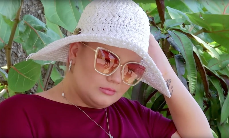 Amber, in a white hat and sunglasses, looks upset