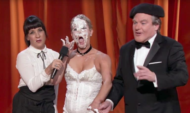 Mike Myers as Tommy Maitland standing next to a cake-eating opera singer on The Gong Show