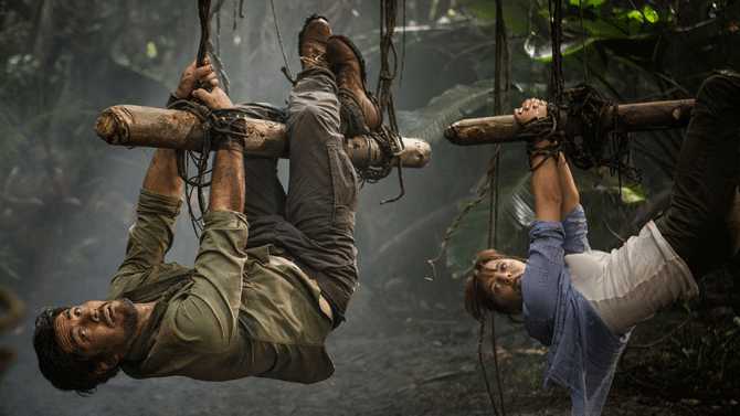 Hooten (Micheal Landes) and Lady Lindo-Parker (Ophelia Lovibond) are tied to logs by their hands and feet in the Amazon jungle and hoisted into the air