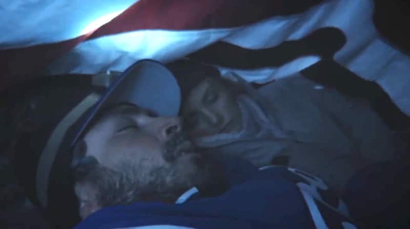 Actors playing Kenny Pasten and Tiffany Finney sheltering under the American flag on In an Instant