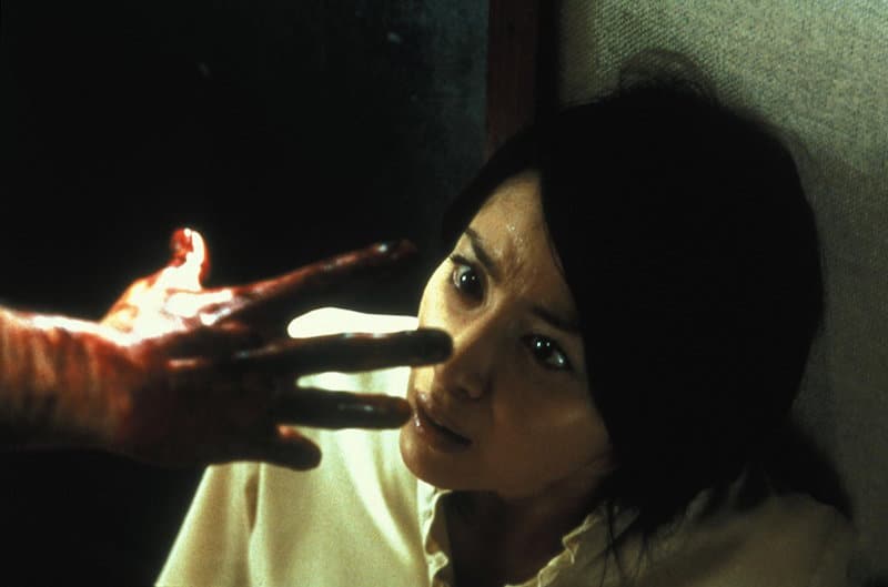 Megumi Okina cowers away from a bloodied hand in Ju-on: The Grudge