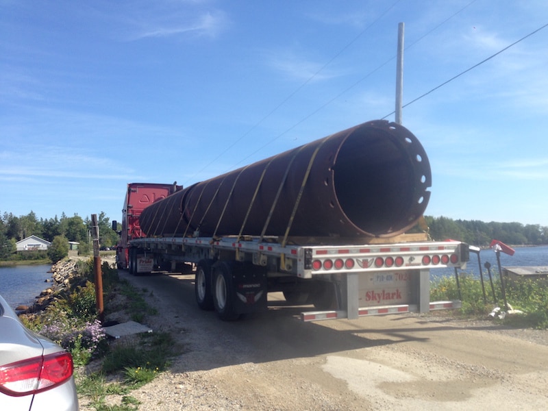 A truck carrying huge metal pipes to Oak Island