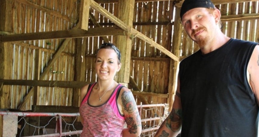 Chico and Sondra smiling in a barn in a still from Discovery's Moonshiners