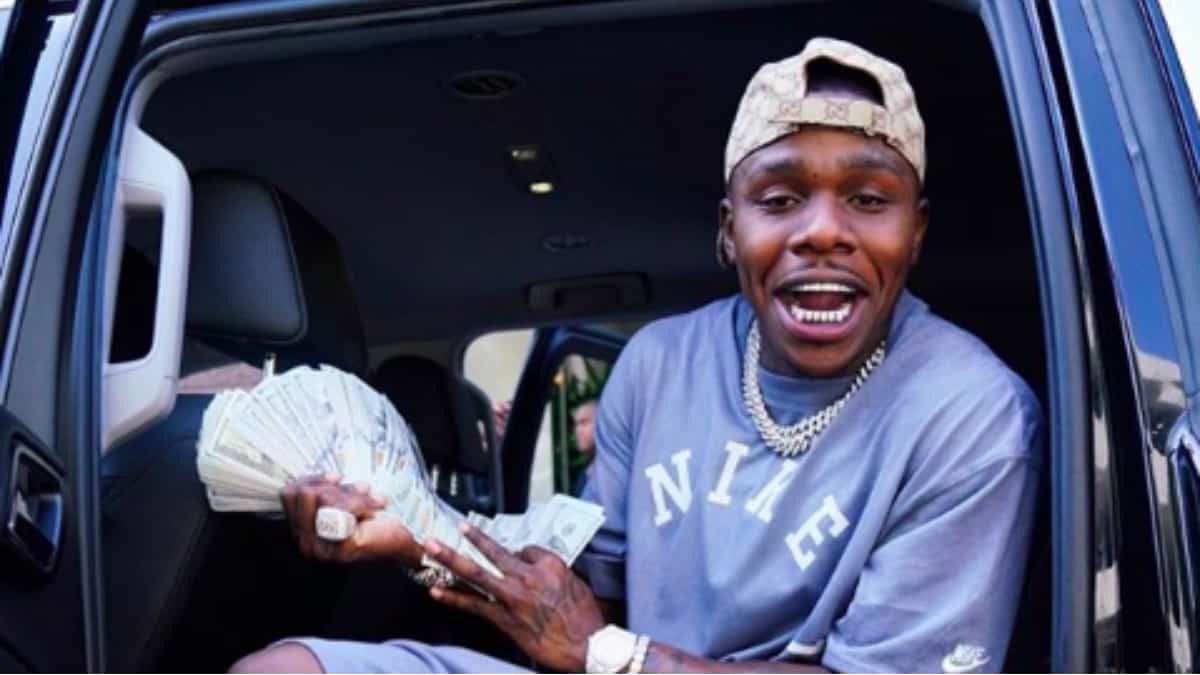 DaBaby posing with money in a car