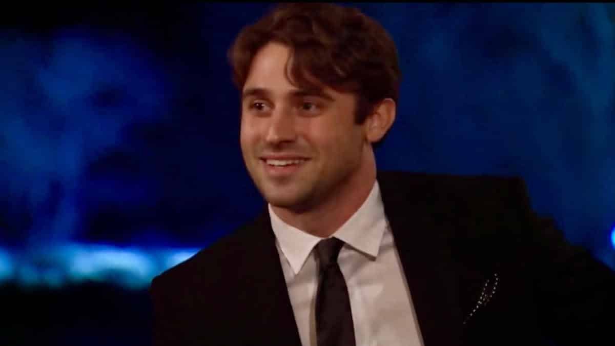 Greg Grippo wears a suit and tie and smiles up at Katie Thurston