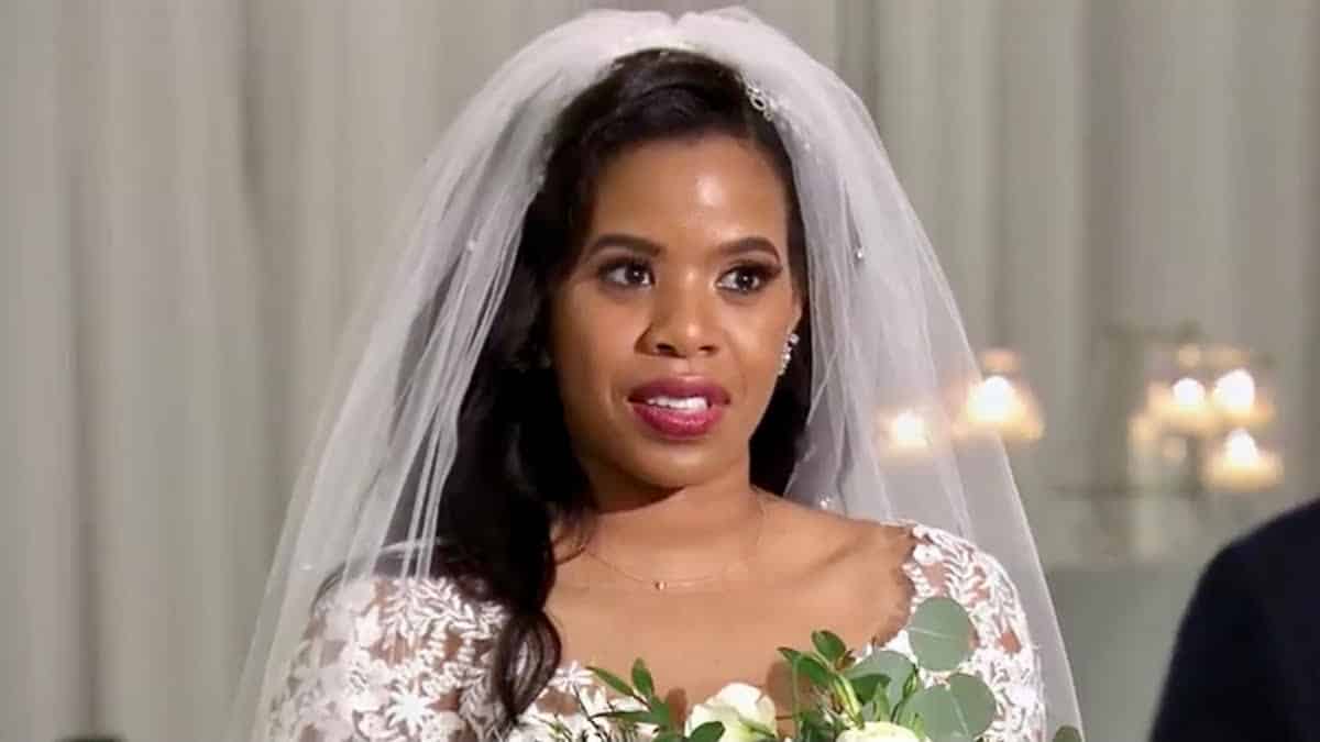 Michaela wears a wedding dress and veil at the altar