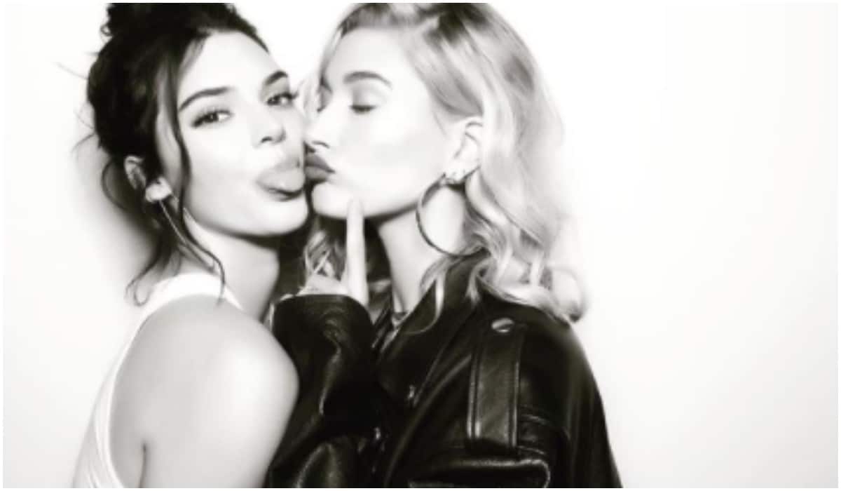 Kendall Jenner sticking her tongue out as Hailey Bieber kisses her cheek.