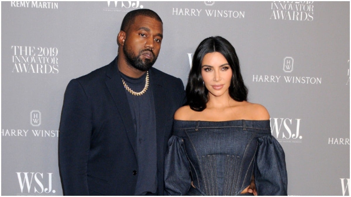 Kanye West and Kim Kardashian wearing dark blue outfits and posing on the red carpet.