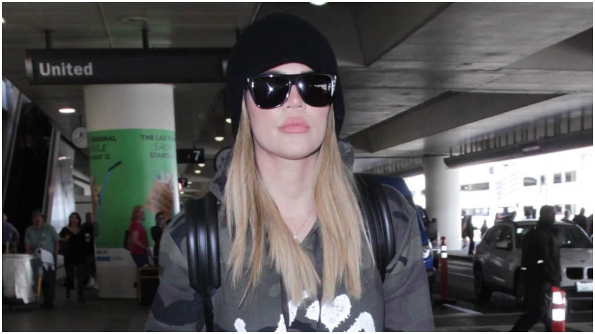 Khloe Kardashian wearing black sunglasses and a grey sweatshirt while walking outside.