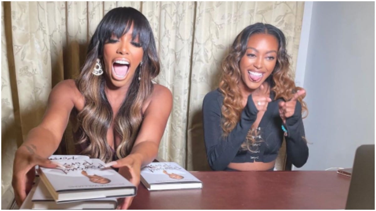 Porsha Williams laughing while holding a stack of books next to her sister, Lauren Williams.