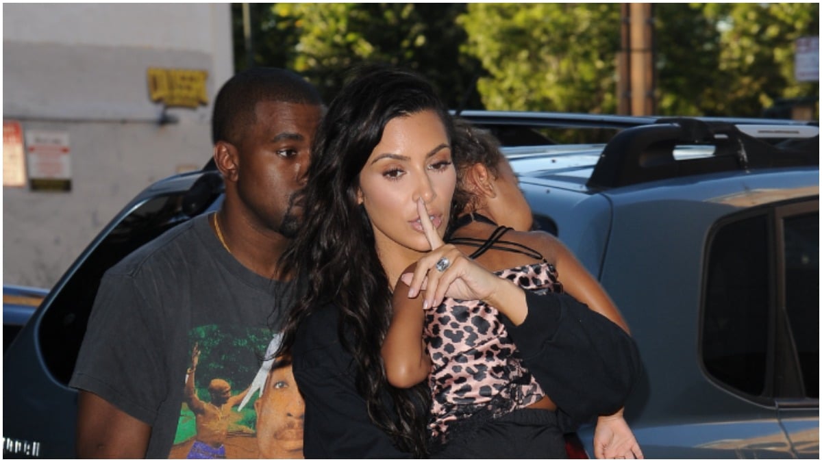 Kim Kardashian putting her finger on her lip while holding North West and walking with Kanye West.