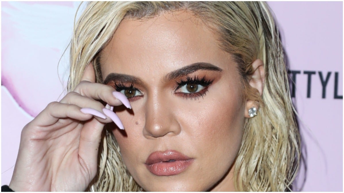 Khloe Kardashian putting one hand in front of her face on the red carpet.
