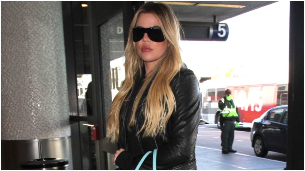 Khloe Kardashian walking outside wearing sunglasses and a hoodie.