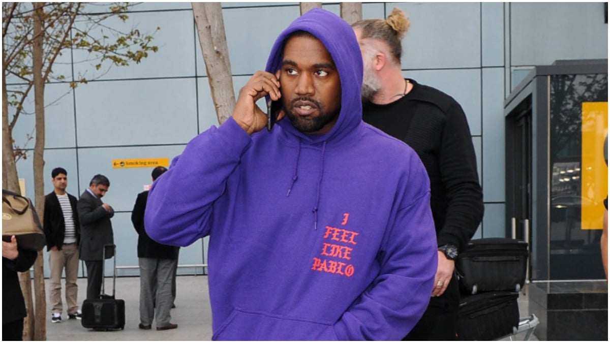 Kanye West talking on the phone in a purple hoodie.
