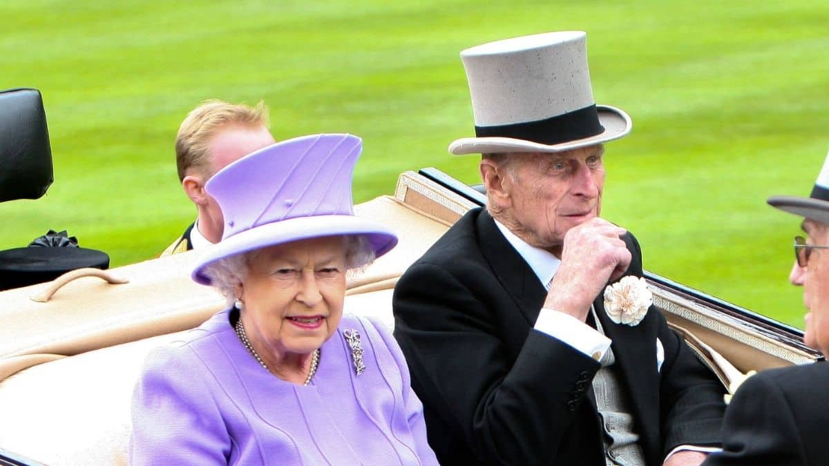 Queen Elizabeth in purple and Prince Philip in a suit riding in a carriage
