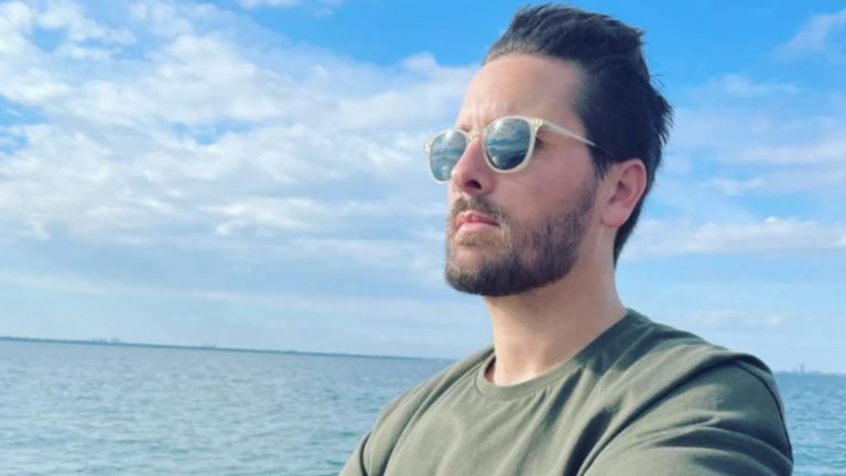 Scott Disick wearing glasses in front of the water with his hair blowing in the wind