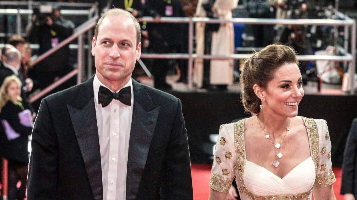 Prince William in a suit with a bow tie and Kate Middleton in a white and gold gown at a movie premiere