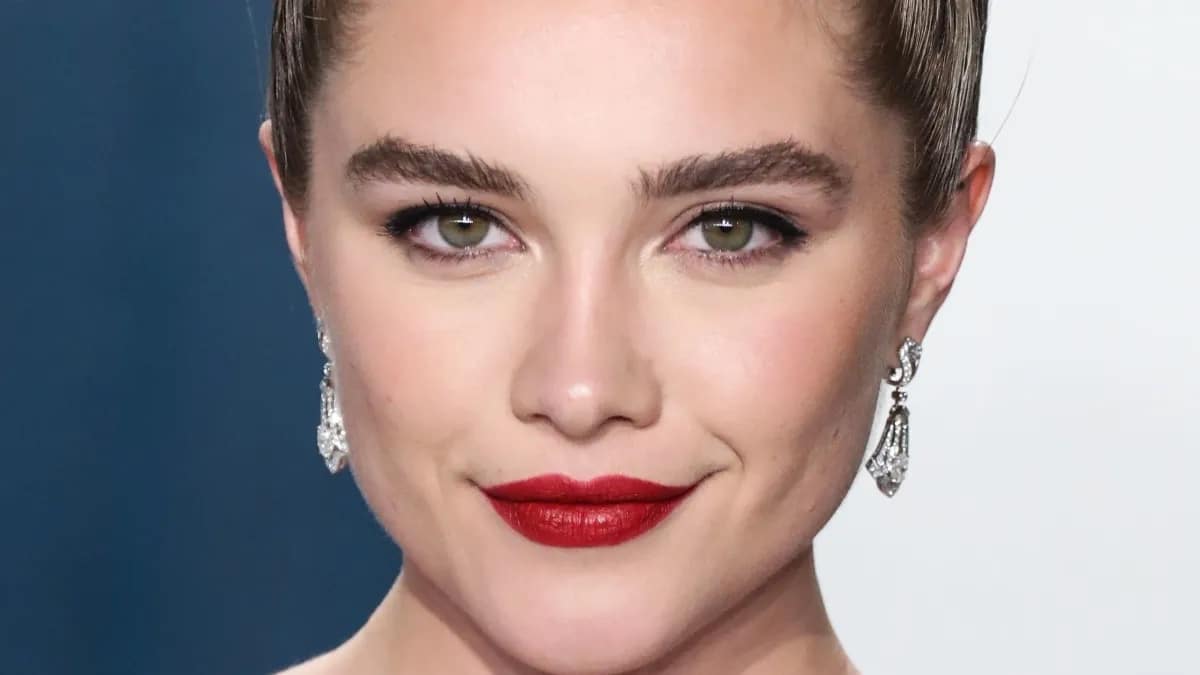Florence Pugh smiles with closed lips in red lip color.