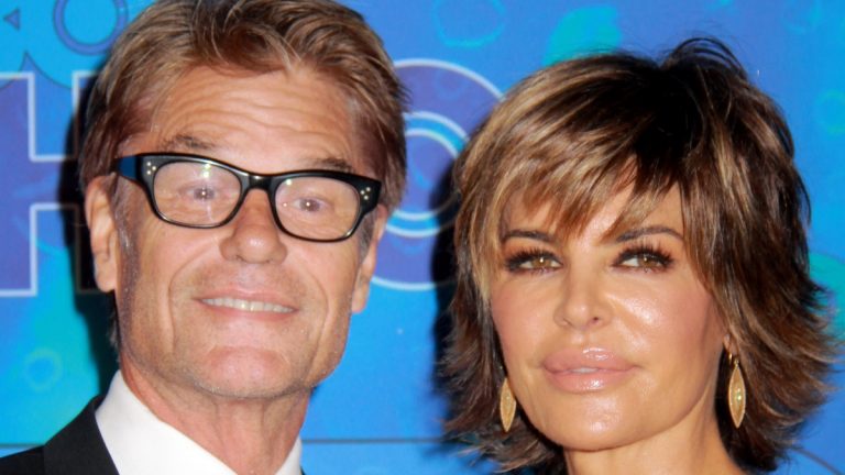 Lisa Rinna and Harry Hamlin smile on the red carpet against a blue background.