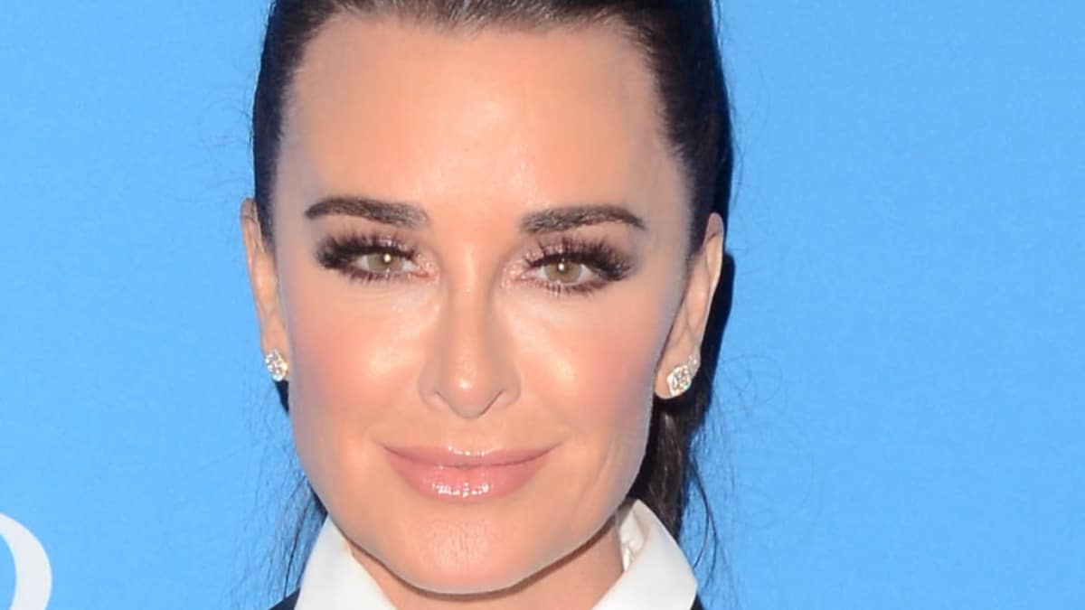 Kyle Richards smiles at the American Woman premiere against a blue background.