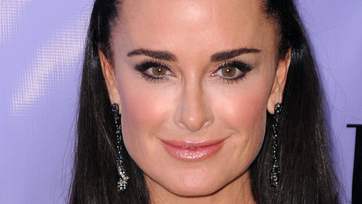 Kyle Richards smiles against a purple background on the red carpet.