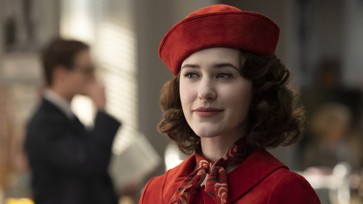 Rachel Brosnahan as Miriam (Midge) Maisel wearing a red jacket with a matching pillbox hat and scarf in the Prime Video series, The Marvelous Maisel.